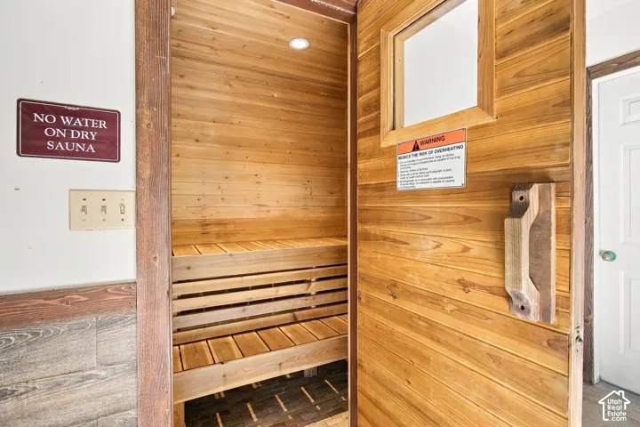 Sauna featuring tongue-and-groove wood paneling, multi-level slatted wood benches, recessed lighting, and a wood-framed door with a glass window