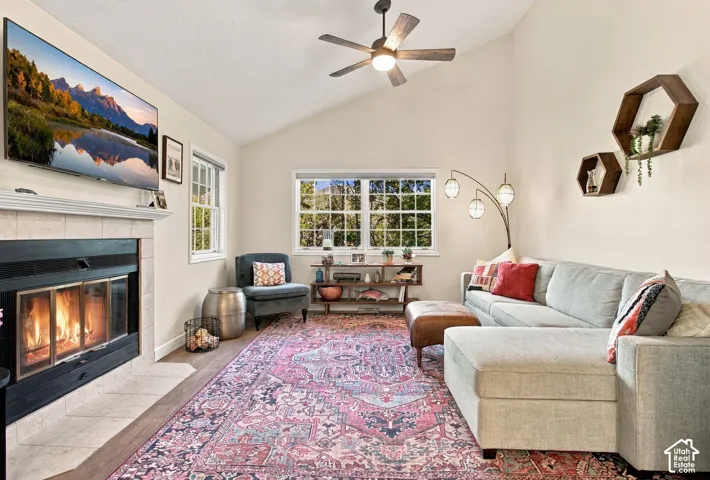 Vaulted ceilings, fireplace with tile surround, multi-pane windows, wood-finish flooring, and integrated ceiling fan