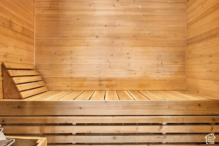 Sauna featuring natural wood-plank wall paneling, tiered bench seating, and a built-in slatted headrest
