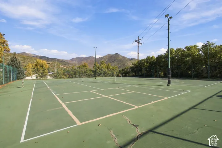 Hard-surface tennis court featuring perimeter chain-link fencing, overhead stadium lighting, and mountain scenery