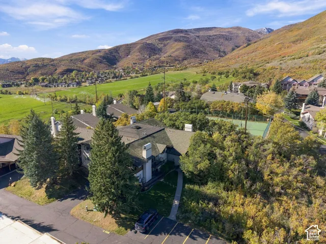 Aerial perspective of a multi-unit property featuring shingle roofing, exterior chimneys, a tennis court, and mature landscaping set against a mountainous backdrop