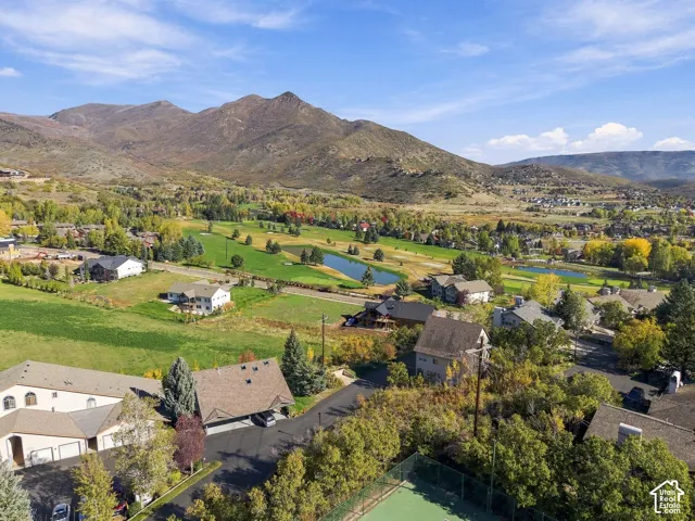 Aerial perspective showcasing a fenced tennis court with a mountain backdrop, situated within a landscape of mature trees and surrounding green space