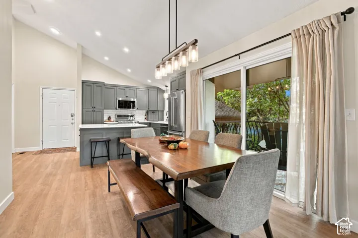 Vaulted ceiling, wood-finish flooring, shaker-style cabinetry, stainless steel appliances, and a linear multi-light pendant fixture