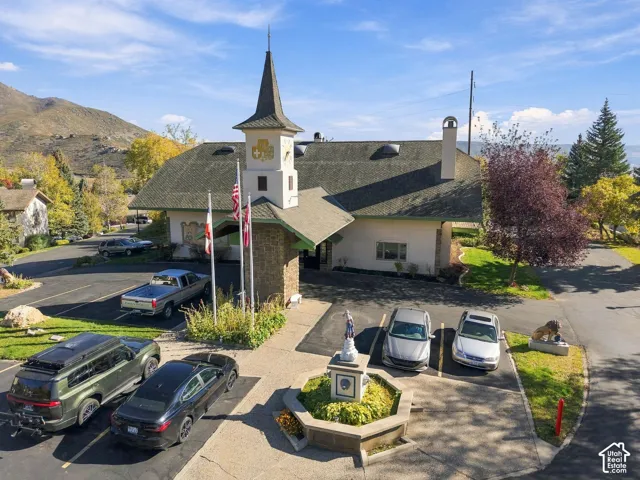 Exterior elevation featuring a prominent central steeple, stone-clad entryway, paved parking area, and an ornamental octagonal fountain