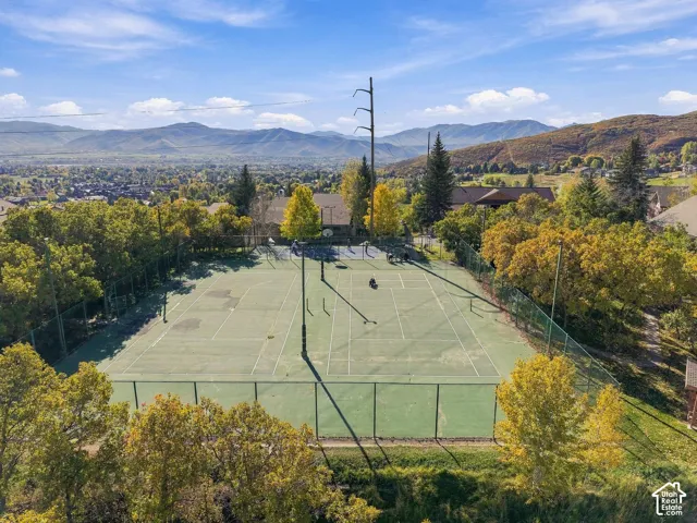 Fenced-in tennis court featuring a hard surface, surrounding trees, and a backdrop of mountain scenery