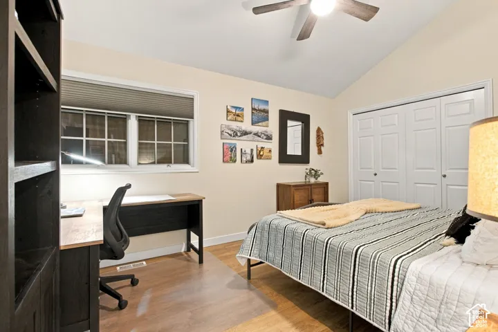 Vaulted ceiling featuring a central wood-finish paddle ceiling fan, dual-pane window with interior shade, and double-door closet with paneled detailing and wood-finish flooring