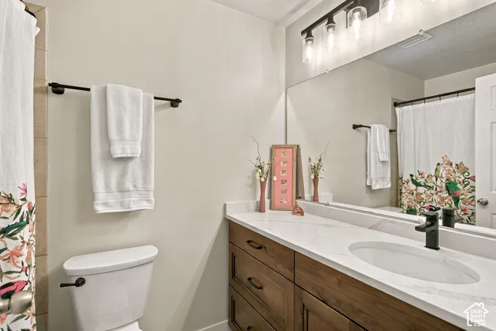 Bathroom vanity featuring a light-toned countertop, under-mount oval sink, matte black faucet, dark wood-finish cabinetry, and a multi-light fixture