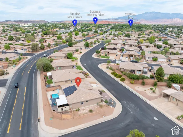 Aerial perspective of a property featuring roof-mounted solar panels, a private swimming pool, a covered patio structure, and surrounding desert mountain scenery