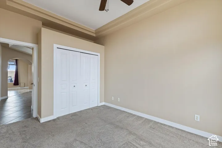 Room featuring a tray ceiling, ceiling fan, neutral carpeting, and a built-in closet with white paneled bi-fold doors