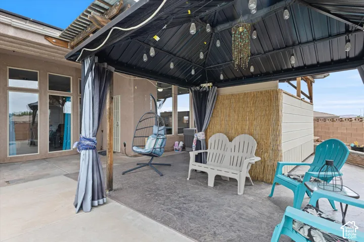 Covered outdoor patio area featuring a metal-frame gazebo, concrete flooring, and privacy paneling
