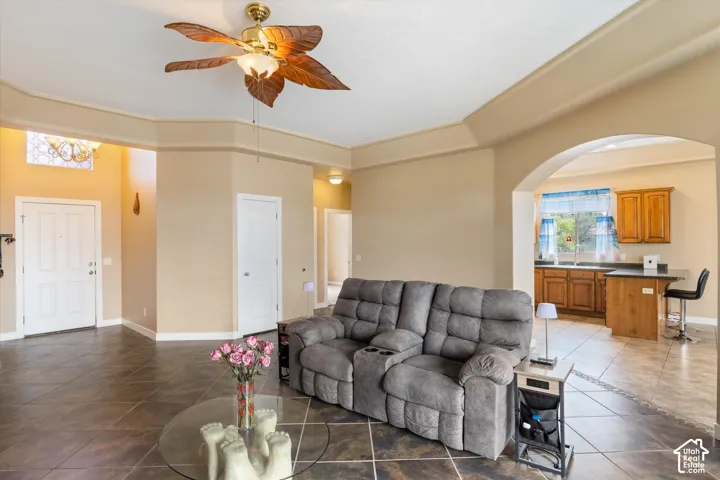 Open floor plan featuring tile flooring, vaulted ceilings, a ceiling fan with leaf-motif blades, an arched pass-through, and kitchen cabinetry with a peninsula