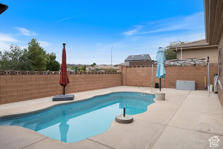 In-ground swimming pool with contoured edges, expansive concrete decking, and decorative masonry perimeter wall