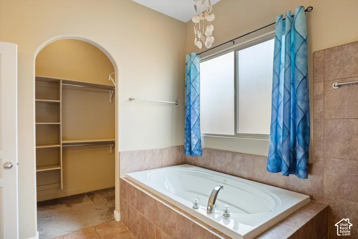 Built-in soaking tub with a tiled surround, arched doorway leading to a walk-in storage area with integrated shelving, and frosted slider window