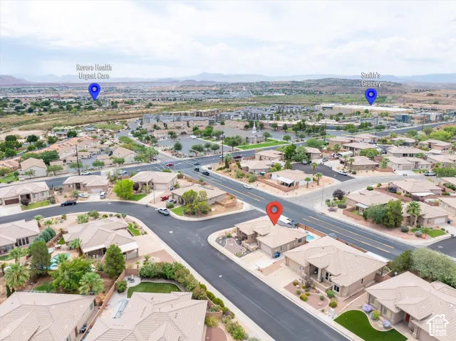 Aerial perspective of a suburban neighborhood featuring single-story residences with tile roofing, paved streets, and a desert landscape backdrop