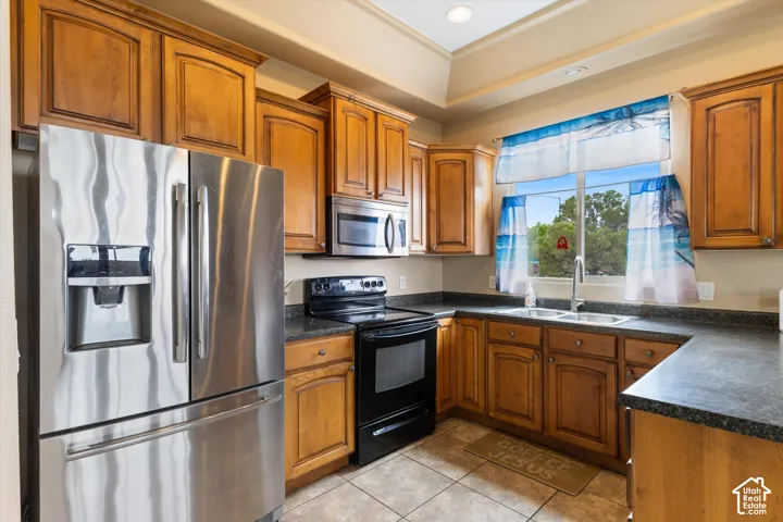 Kitchen featuring wood cabinetry, stainless steel refrigerator, black electric range, tray ceiling with recessed lighting, and tile flooring