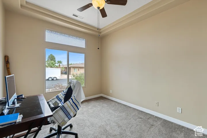 Tray ceiling featuring a central ceiling fan with integrated lighting, oversized window with a textured transom, and neutral carpeting