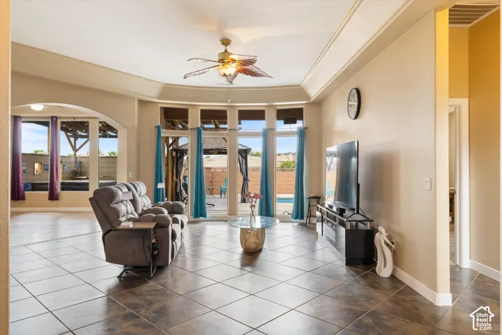 Living area featuring tile flooring, tray ceilings, recessed lighting, a ceiling fan, and large windows