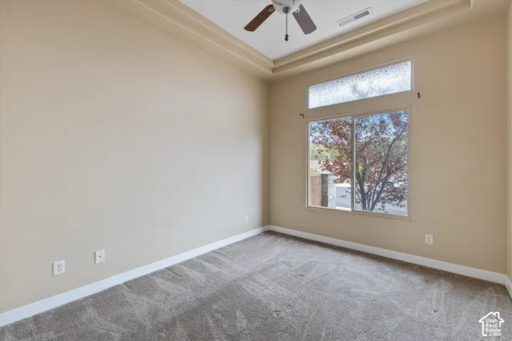 Room featuring a trey ceiling, neutral carpeting, a ceiling fan with integrated lighting, and a window with a transom light