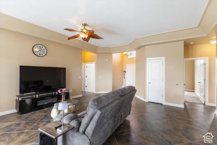 Interior space featuring high tray ceilings, neutral wall tones, large-format tile flooring, and a ceiling fan with integrated lighting