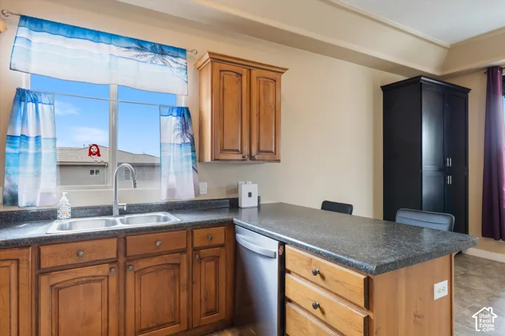 Kitchen area featuring wood cabinetry, solid surface countertops, a stainless steel dual-basin sink with a gooseneck faucet, integrated dishwasher, and a floor-to-ceiling dark wood storage cabinet
