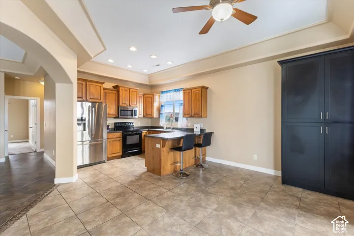 Kitchen featuring wood cabinetry, a breakfast bar, stainless steel appliances, tile flooring, and a tray ceiling