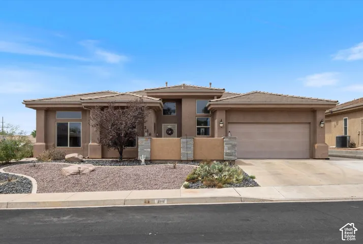 Stucco exterior featuring stacked stone accents, a multi-car garage, and xeriscaped front yard landscaping