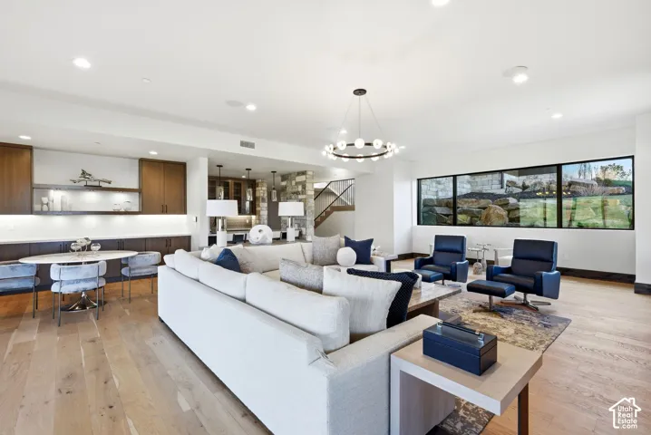 Expansive open-concept living area featuring light wood-finish flooring, a contemporary chandelier, and recessed lighting