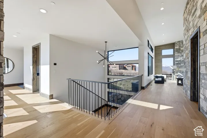 Open-concept upper-level landing featuring light wood-finish flooring, a contemporary black metal railing, a modern chandelier, recessed lighting, and expansive windows