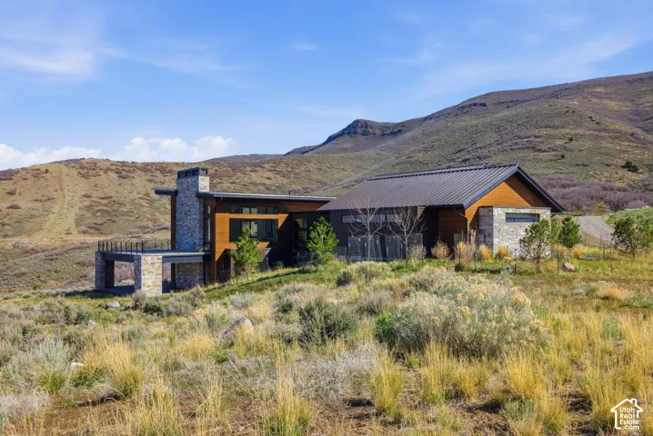 Contemporary exterior design featuring a stone facade, wood-panel accents, large windows, and a metal roof