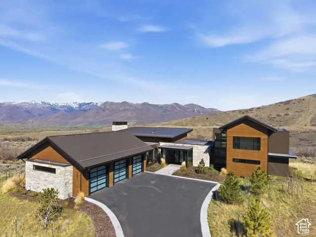 Contemporary mountain residence featuring a stone and wood-finish exterior, a multi-car garage with frosted glass doors, and a paved driveway