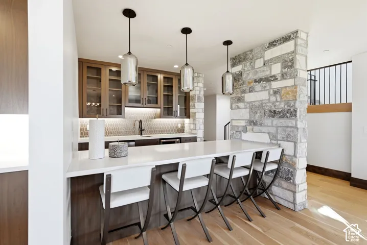Custom wet bar featuring wood-finish cabinetry with glass fronts, a tile backsplash, and under-cabinet lighting