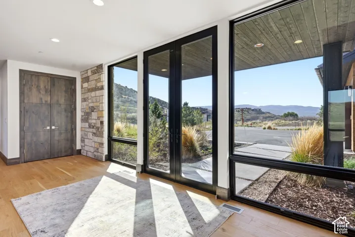 Floor-to-ceiling windows with black frames, wood-finish flooring, recessed lighting, and a stone accent wall