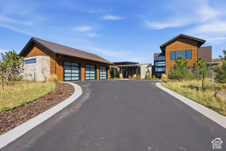 Paved driveway with a concrete border leading to a modern residence featuring stone and wood siding, a metal roof, and large windows