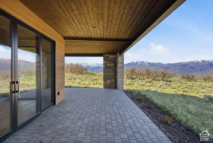 Expansive outdoor patio featuring gray paver flooring, a wood-planked ceiling, and a stone column