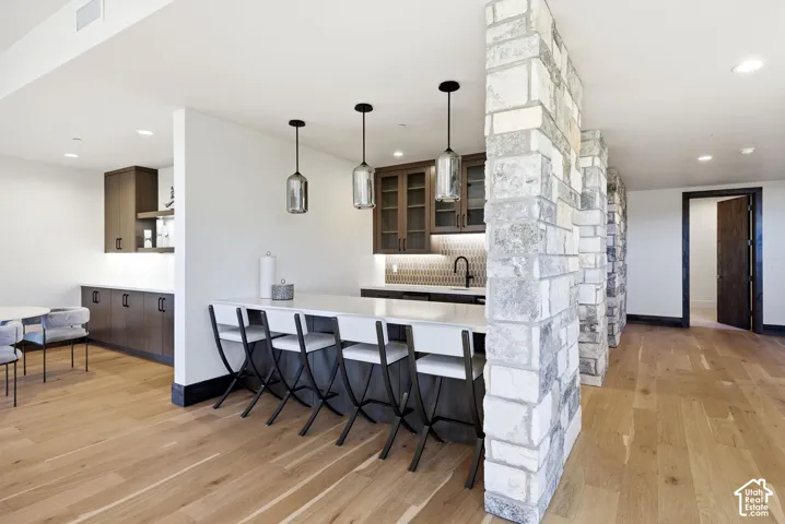 Modern kitchen featuring a breakfast bar with seating, pendant lighting, wood-finish flooring, and stone accent pillars