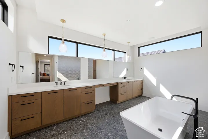 Freestanding soaking tub with a matte black floor-mounted faucet, complemented by a dual vanity featuring light wood-finish cabinetry, white countertops, and black hardware