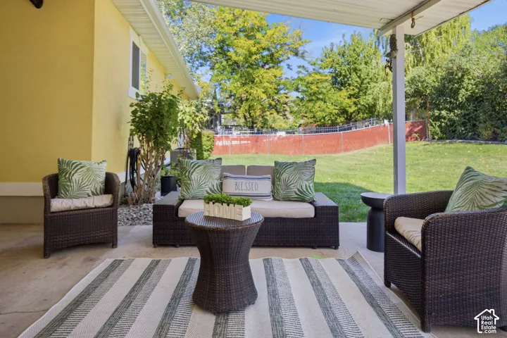 Covered concrete patio featuring a support pillar and a large, fenced-in backyard with a grass lawn