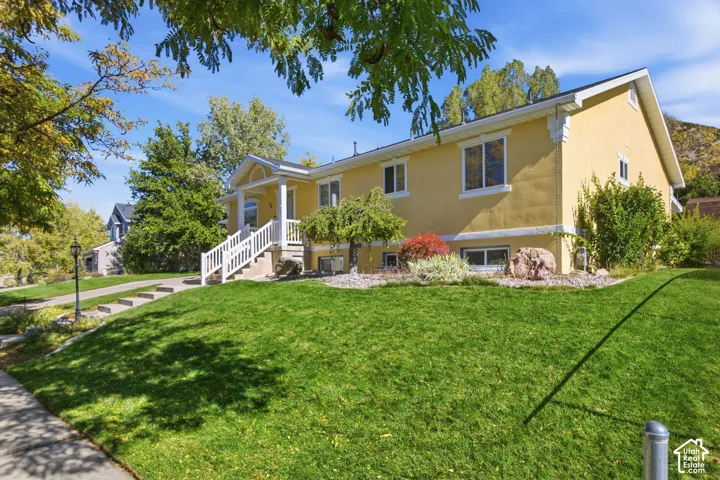 Stucco exterior with decorative corbels, white-railed entrance staircase, concrete walkway, and landscaped front yard with stone accents