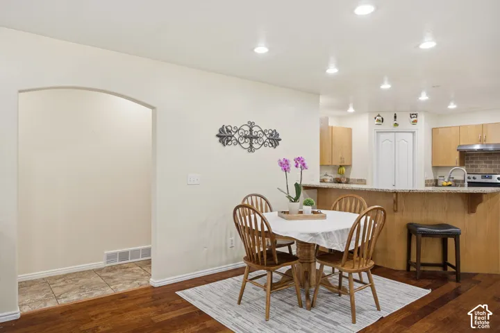 Kitchen featuring wood-finish cabinetry, stone-style countertops, recessed ceiling lighting, and wood-finish flooring with a distinctive arched doorway