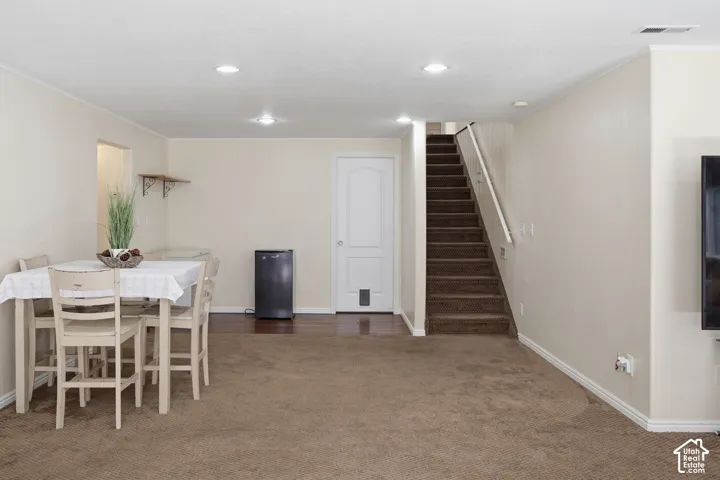 Neutral-toned interior space featuring recessed lighting, carpeted flooring, wood-finish flooring, and a carpeted staircase with a white handrail