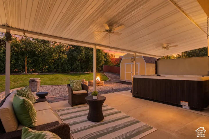 Covered concrete patio featuring ceiling-mounted fans, an integrated spa, a circular stone fire pit, and a detached storage shed