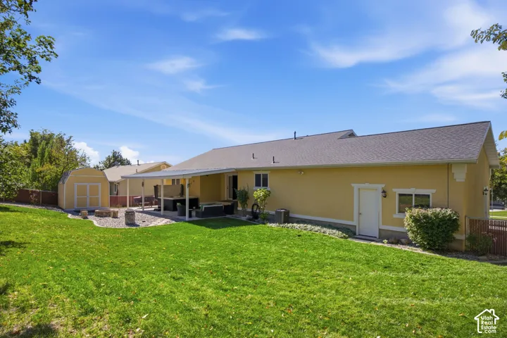 Backyard featuring a manicured lawn, stone-surfaced hardscaping, covered patio, and detached storage structure
