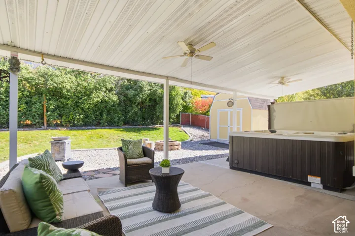 Covered concrete patio featuring ceiling fans, a built-in spa, and hardscaped yard area with a detached storage shed