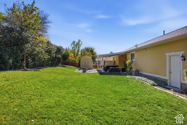 Expansive backyard featuring a manicured lawn, mature trees, a detached storage shed, and a covered patio
