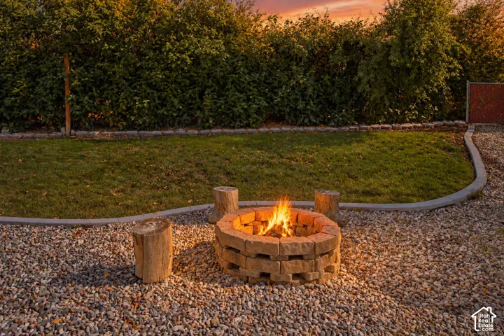Backyard area featuring a circular stone fire pit, gravel ground cover, manicured lawn, concrete curbing, and perimeter landscaping
