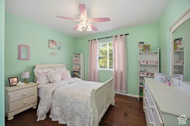 Bedroom featuring dark wood-finish flooring, a multi-blade ceiling fan with integrated light fixture, and a window with horizontal blinds