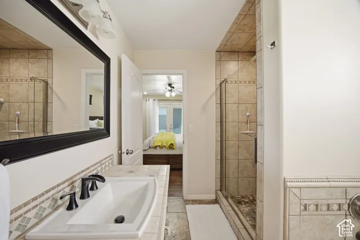 Bathroom featuring a tiled vanity countertop with an integrated basin, a black-framed mirror, a glass-enclosed shower with tiled walls, and a decorative tile backsplash