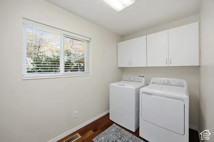 Laundry room featuring wood-finish flooring, white wall-mounted cabinetry, and a horizontal window