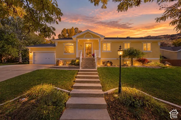 Single-story exterior featuring light-toned stucco siding, a covered entryway with a gabled porch, concrete stairs, a concrete driveway, and an attached two-car garage