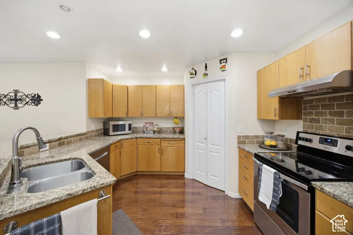 Kitchen featuring natural wood cabinetry, stone-patterned countertops, brick-style backsplash, wood-finish flooring, and stainless steel appliances